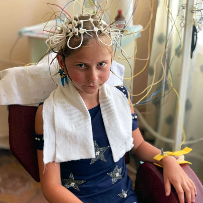Nine-year-old Kristina sits in a chair patiently as a medical device that's placed on her head conducts radiation tests
