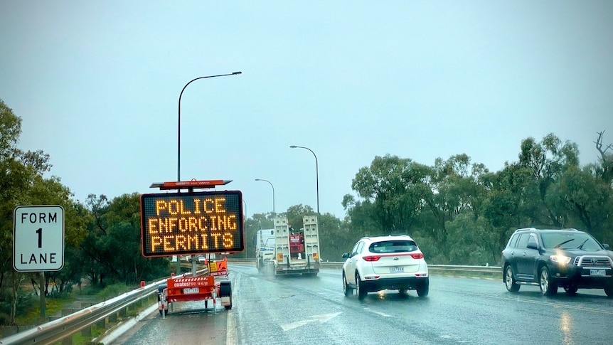 Police enforcing permits sign on border between New South Wales and Victoria. It is raining. 