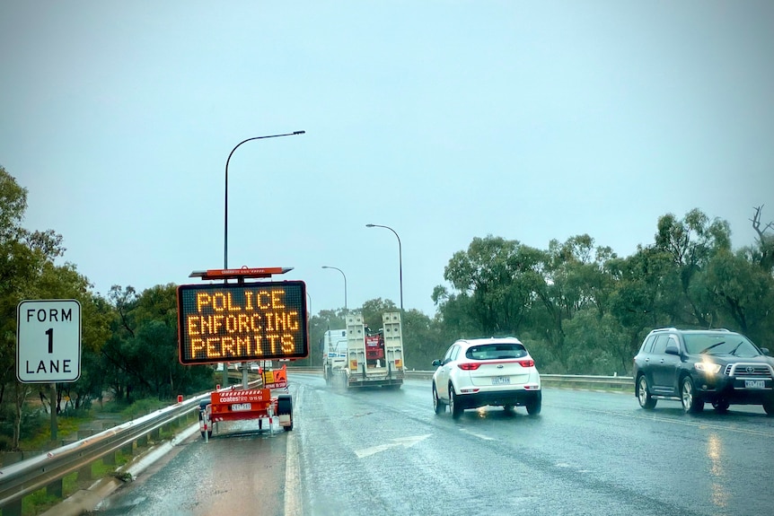 Police enforcing permits sign on border between New South Wales and Victoria. It is raining. 