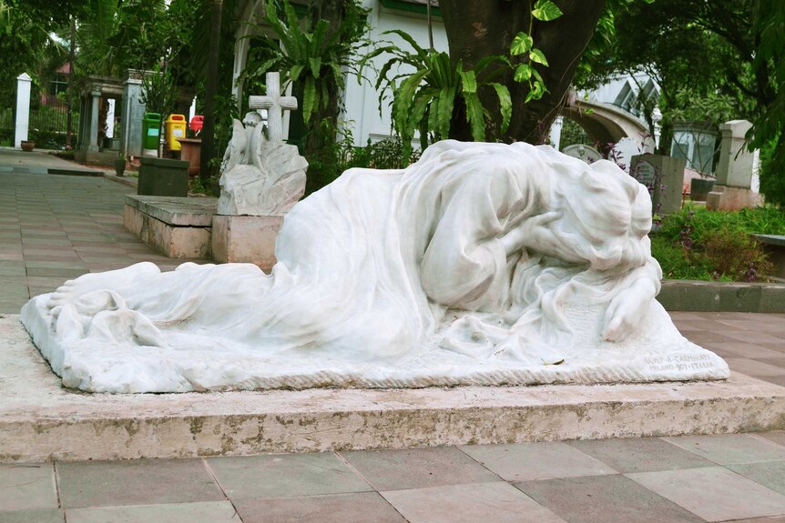 A white statue depicts a woman weeping into her hands, crouched over.