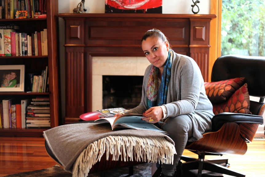 Kristine Becker sitts in a lounge room leafing through a book.