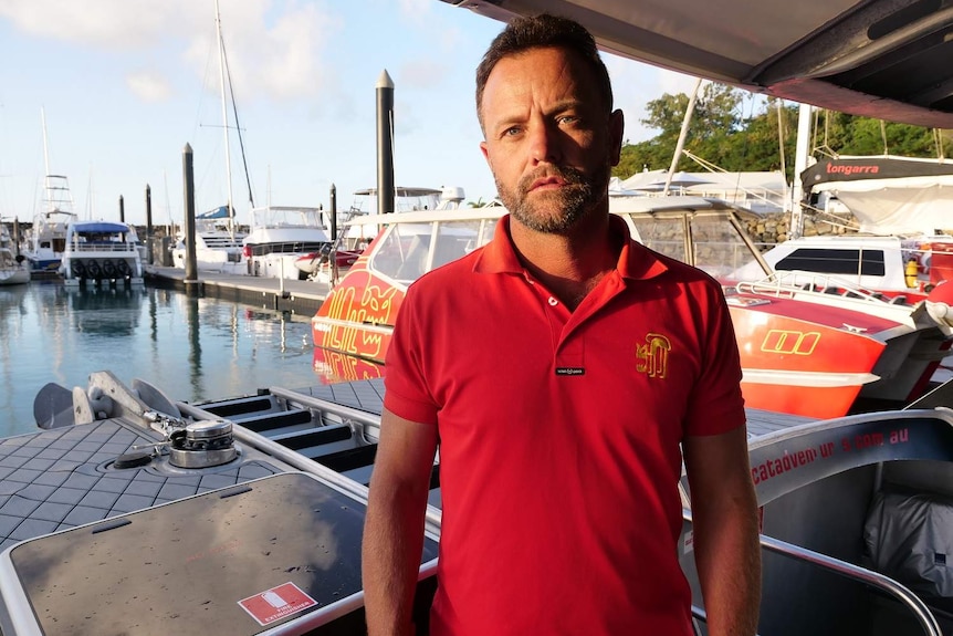 Asher Telford stands on a boat at a marina at Airlie Beach.