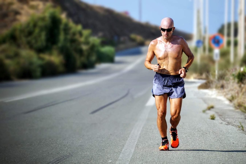 A shirtless man jogs along a road.