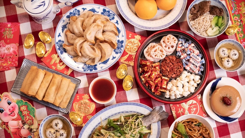 8 lucky Lunar New Year foods including dumplings, spring rolls, oranges, whole fish, year cake and sweet rice dumplings.