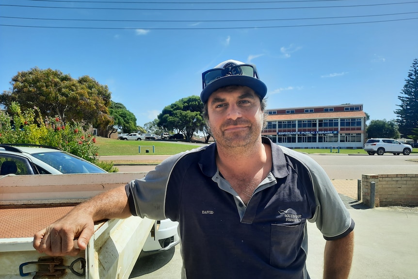 A man leans against the side of a ute tray, with sunglasses pushed to the top of his head.