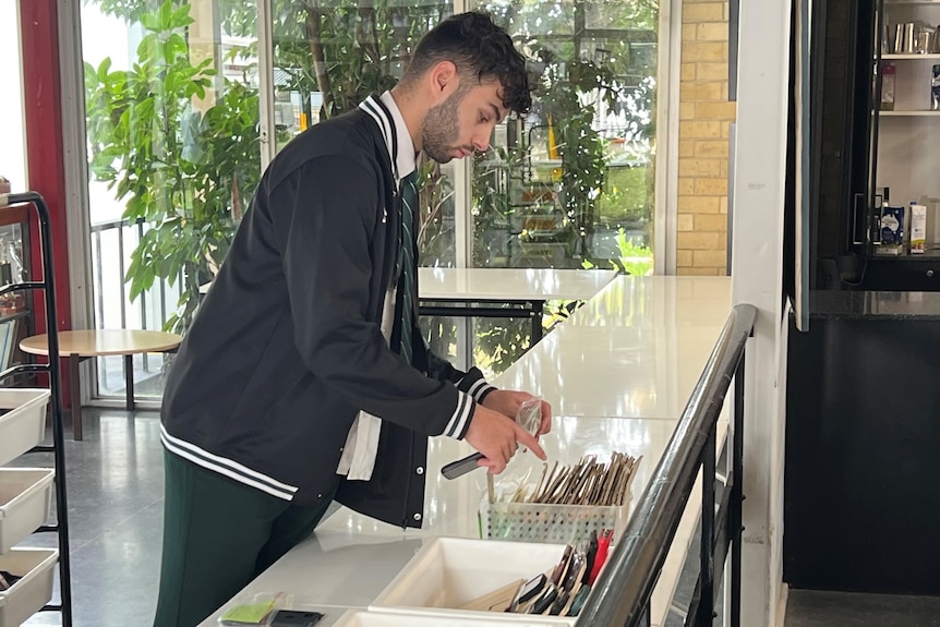 Boy drops mobile phone into clear bag at school foyer