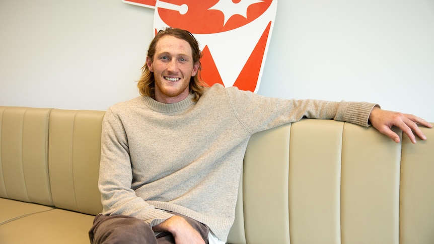 Retiring AFL player Nathan Murphy sitting on a couch wearing a jumper and pants. 