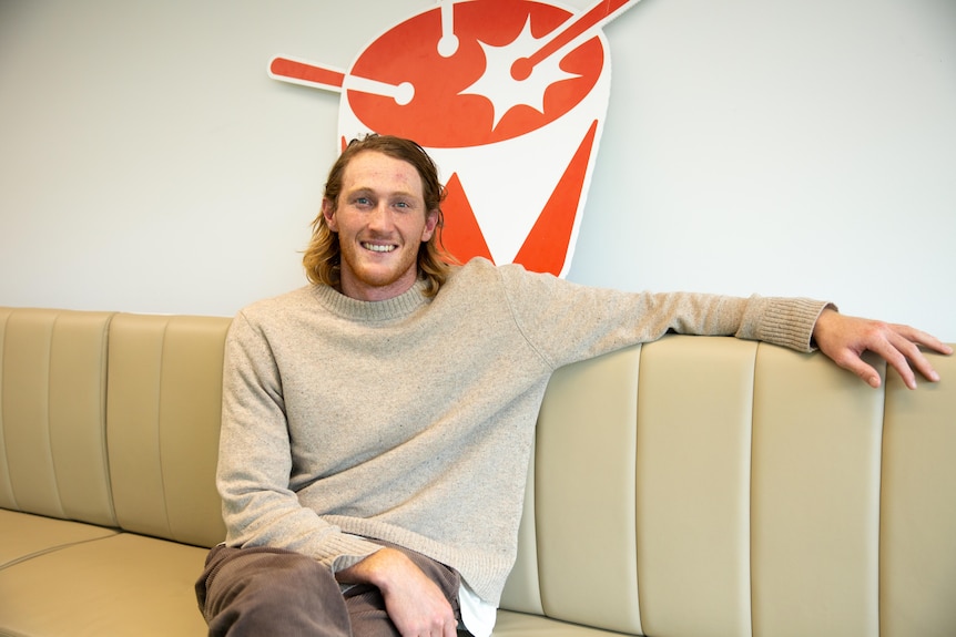 Retiring AFL player Nathan Murphy sitting on a couch wearing a jumper and pants. 