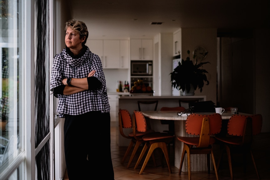 A shadowy wide shot of Renee Pickles looking out her door.