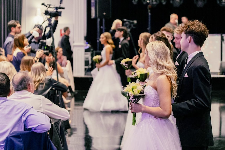 Couples stand on a dance floor in front of professional photographers