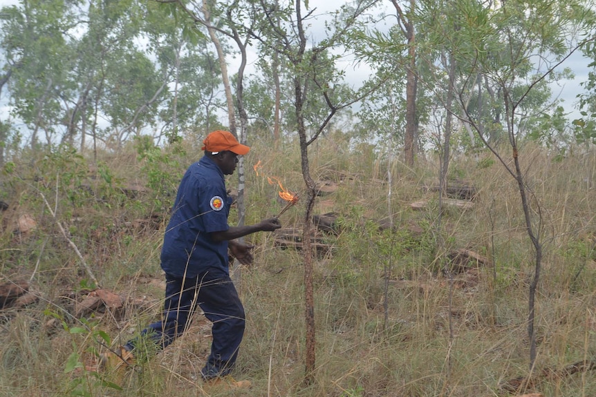 A man walks through dry grassland with a lit torch.