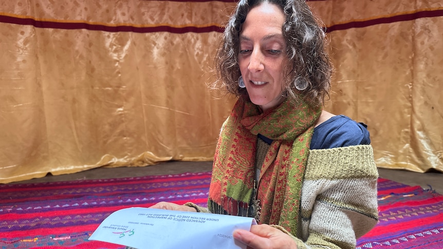 A person reading a letter from their local council, sitting inside a yurt.