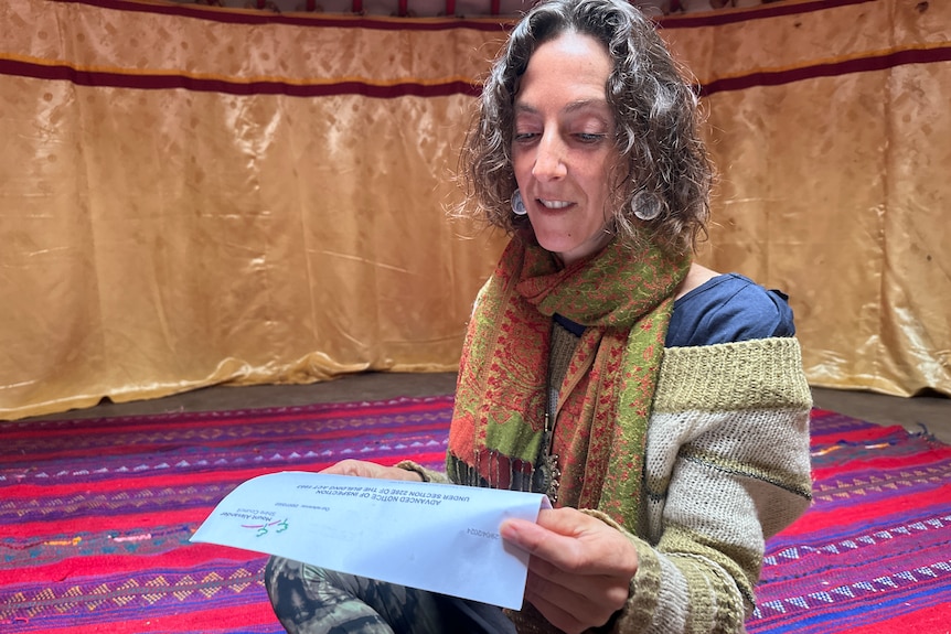 A woman with curly hair reads a letter, which sitting inside a yurt.