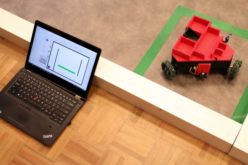 A laptop sits beside a red three wheeled car robot