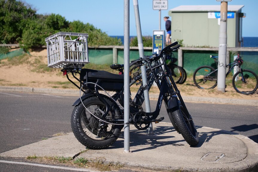 A bike with fat tyres lean against a pole at the beach.