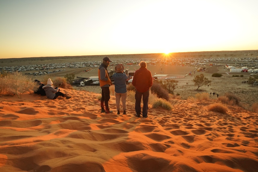 Three people standing on sand dune watching sunrise