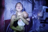 A young Asian woman in a black singlet holds a baby to her chest and cries 