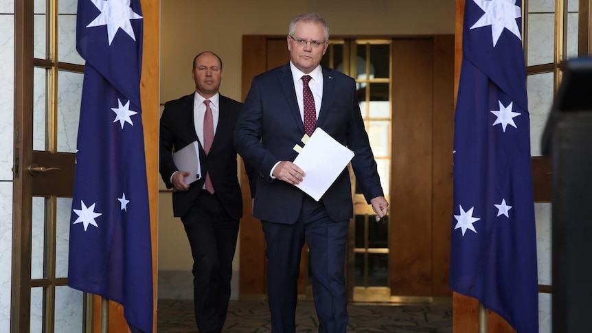 Both men walk out through the open doorway between two Australian flags.