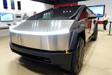 A close up photo of the front of a Tesla Cybertruck in a showroom, with some people standing behind it
