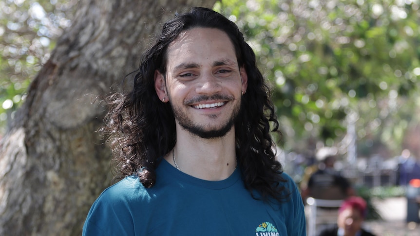 Young Indigenous man with long black curly hair smiles at camera