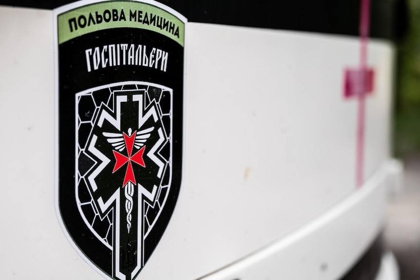 A close-up on an insignia on a white bus. It's a black crest with words in Russian Cyrillic alphabet