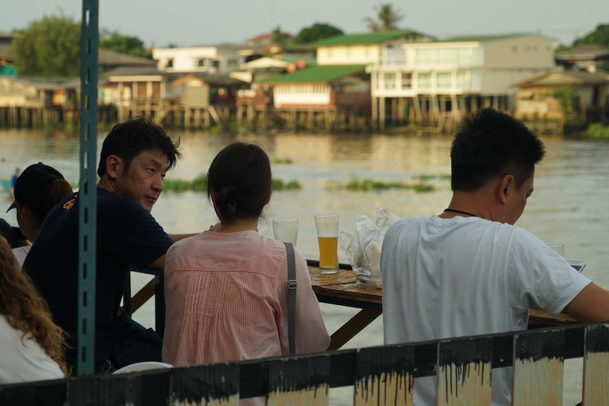 Two men and a women drink beer at Chit's Beer bar, overlooking a river in Koh Kret, Thailand.