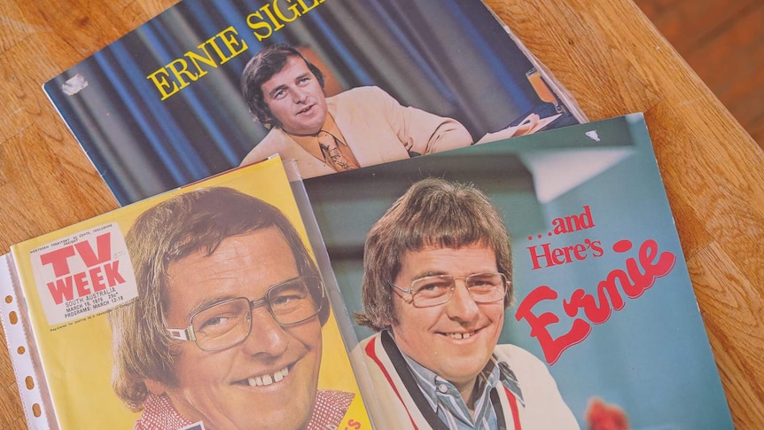 An old magazine and two records with Ernie Sigley's face and name on their covers sit on a wooden table.