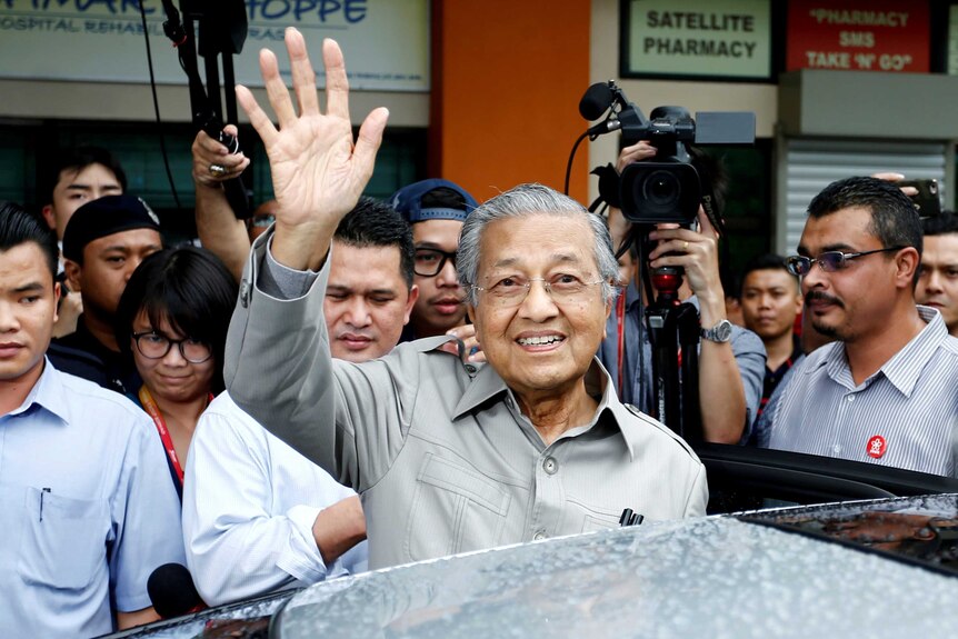 Former Malaysian Prime Minister Mahathir Mohamad waves as is surrounded by people.