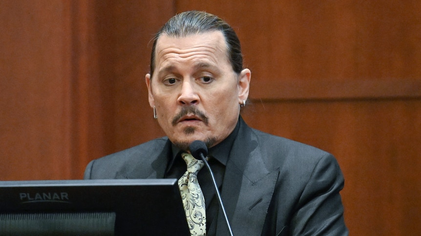 Man in a black shirt and green tie testifies in court.