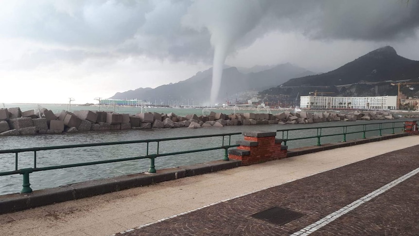 A photo taken from the road looking across a bay shows a tornado-like waterspout in the distance.