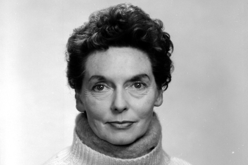 Black and white photo of Nel Law smiling slightly with closed mouth, against plain background, wearing woolen turtleneck jumper.