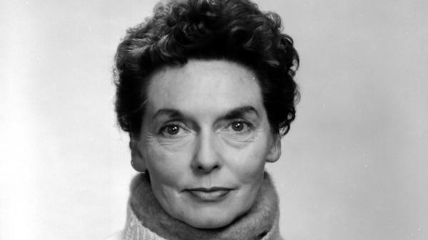 Black and white photo of Nel Law smiling slightly with closed mouth, against plain background, wearing woolen turtleneck jumper.