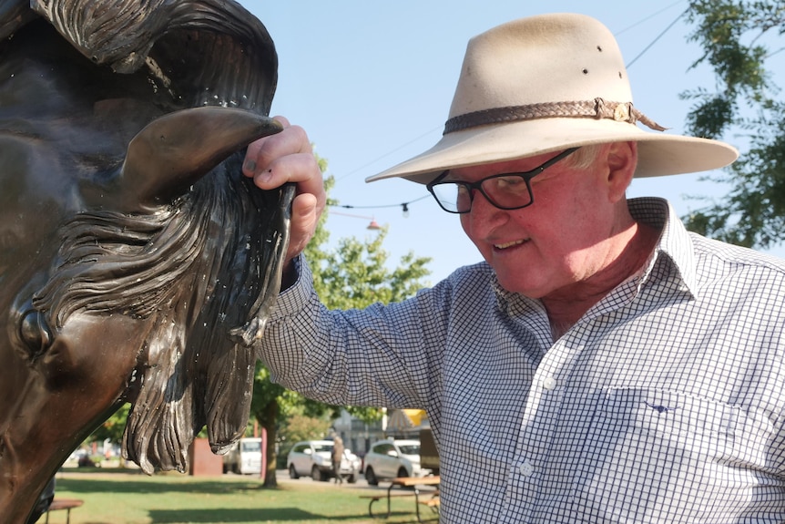 A man in a cowboy hat looks at a horse statue