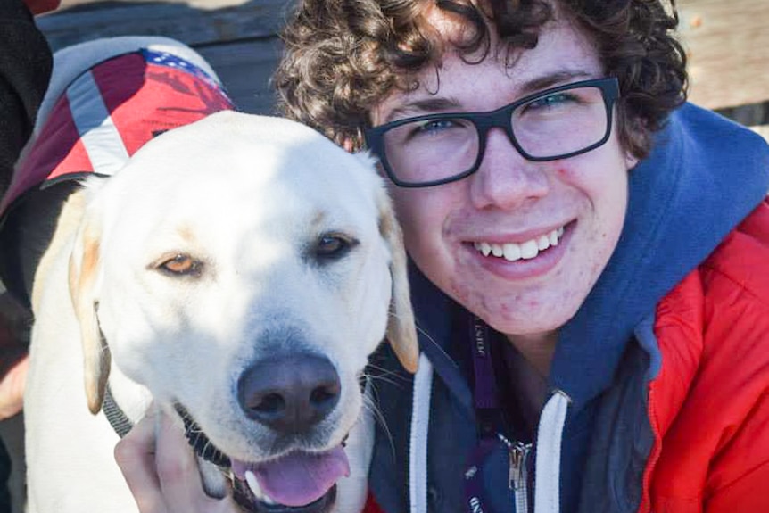 A teenage boy with glasses gets up close to a Labrador dog that looks happy