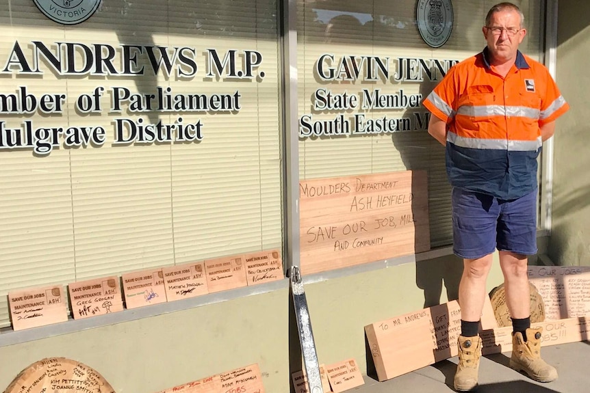 A Heyfield mill worker stands outside MPs' offices with pieces of wood displaying written messages such as "save our jobs".