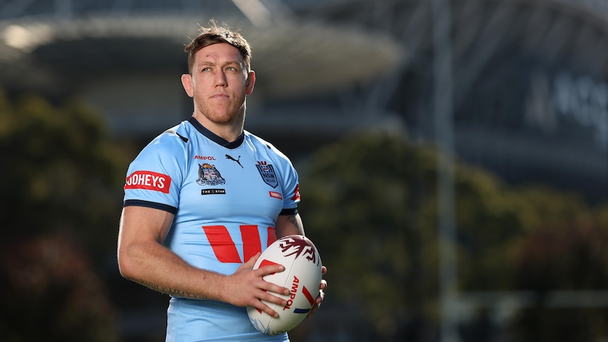 A man poses in a New South Wales jersey before a State of Origin game