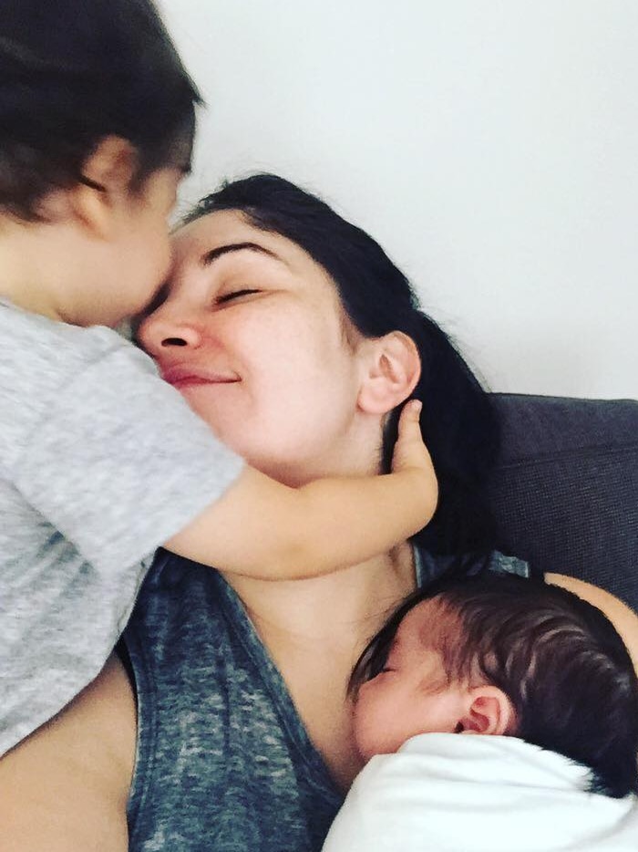 A woman cuddles her newborn daughter and toddler