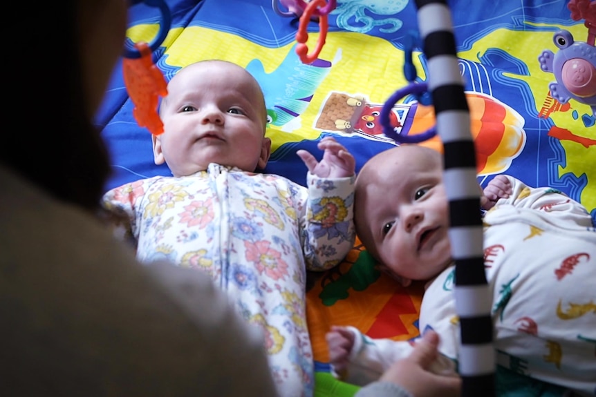 Two babies lie together on a play mat.