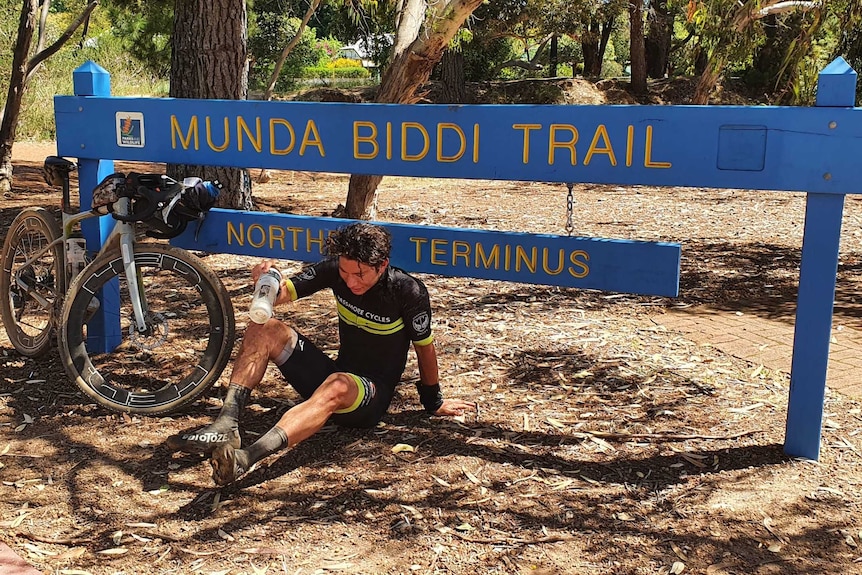 A man sits on the ground next to a bicycle.