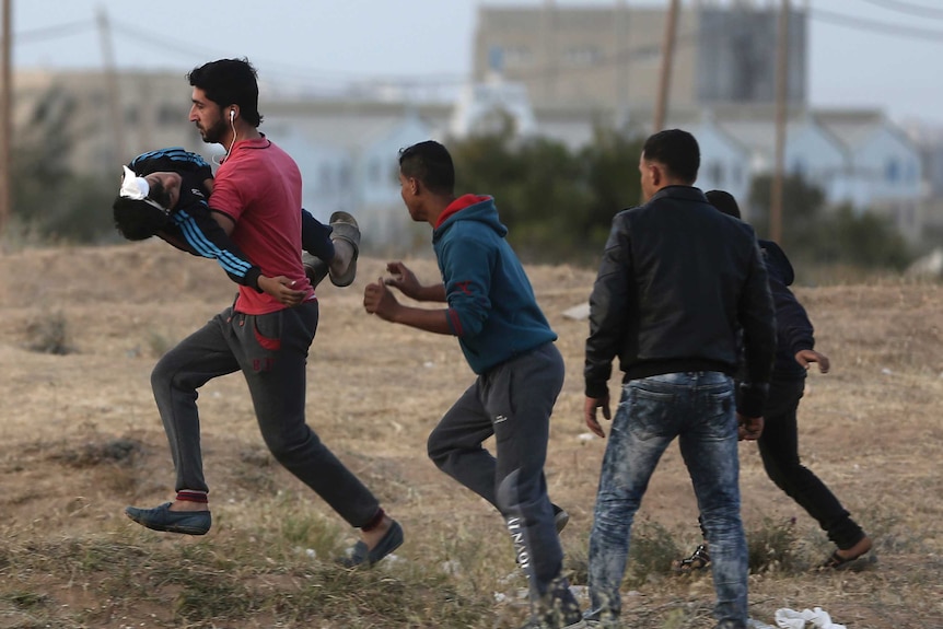 A man is seen carrying a boy who appears to be wounded in the head.