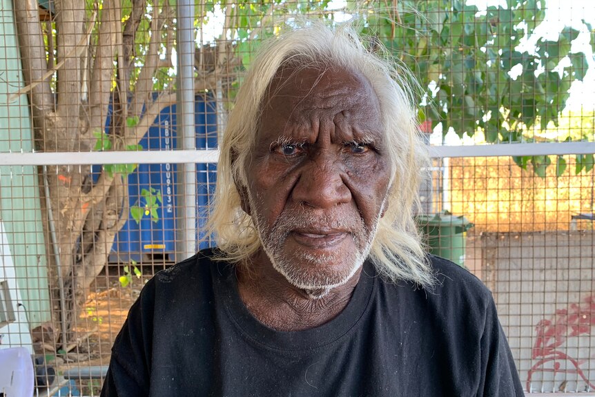 An old Aboriginal man with white hair looks at the camera