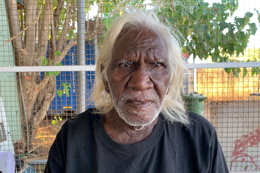 An old Aboriginal man with white hair looks at the camera