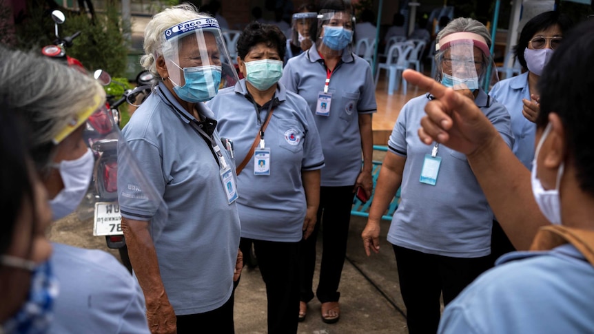 A group of older Thai women in blue polo shirts and clear facial visors