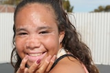 Young woman sits on a trampoline smiling at the camera.