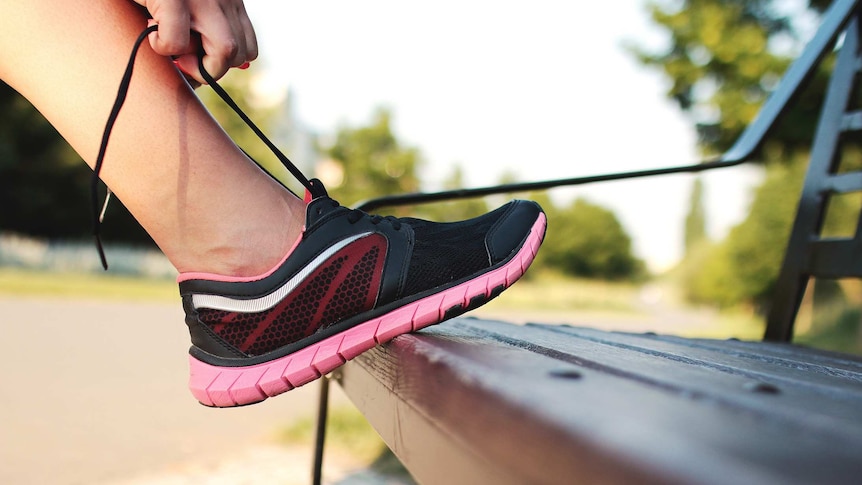 Close-up of a woman tying shoelaces on her running shoes against a park bench.