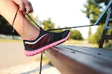 Close-up of a woman tying shoelaces on her running shoes against a park bench.