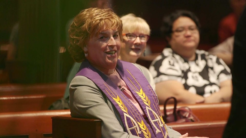 Jo sits in a church pew, smiling towards the camera.