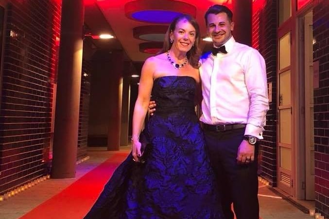 A woman in a ballgown, a man in a suit stand on a red carpet