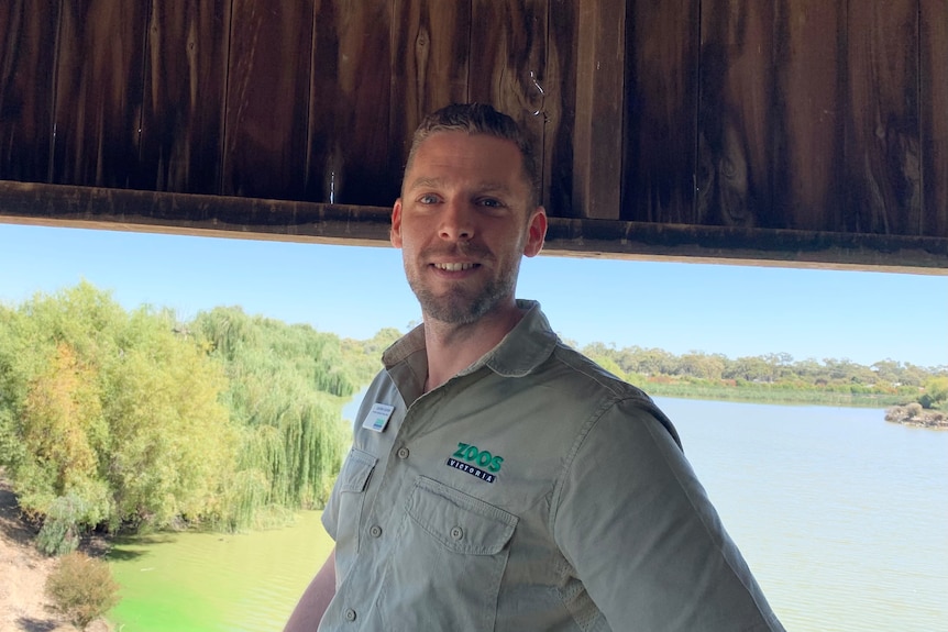 A bearded man with a Zoos Victoria logo on his shirt with lush wetlands in the background.