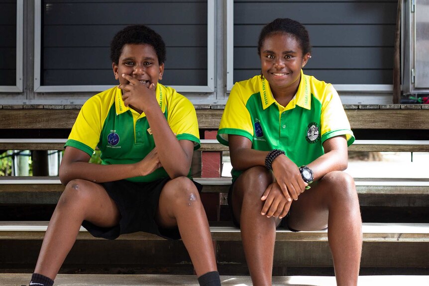 Two school students sit on the steps outside their school.